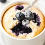 Keto Blueberry Mug Cake: Quick and Delicious Recipe 6 A fluffy keto blueberry mug cake in a white mug topped with fresh blueberries and powdered sweetener.